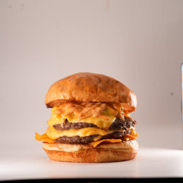 A double patty burger from The Burger Truck, topped with melted cheese, sauce, and tortilla chips.