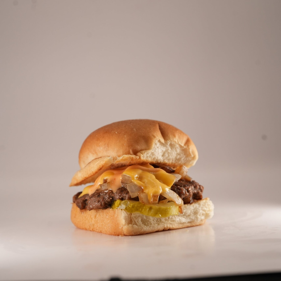 A Burger Truck slider with melted cheese, grilled onions, and pickles on a bun.
