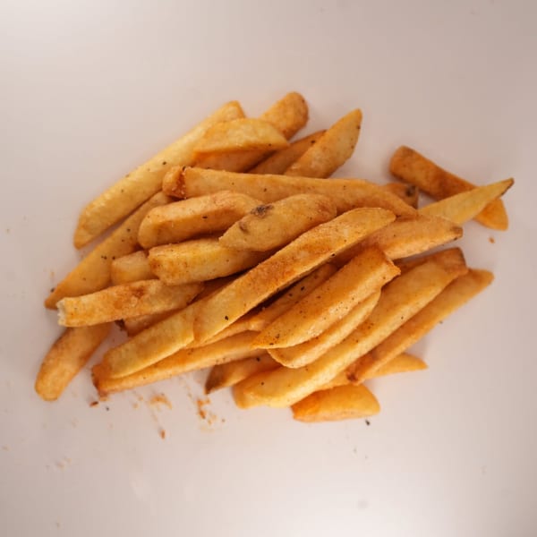 A pile of golden-brown, seasoned french fries from The Burger Truck on a white surface.
