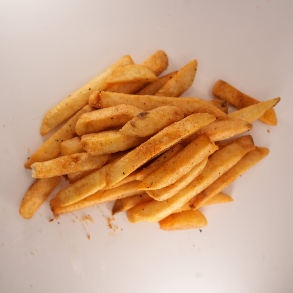 A pile of golden-brown, seasoned french fries from The Burger Truck on a white surface.