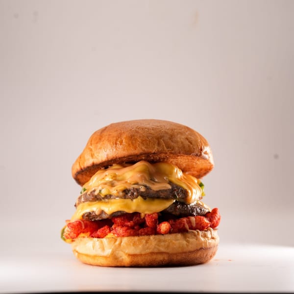 A double cheeseburger from The Burger Truck, topped with melted cheese, sauce, and crunchy red snacks.