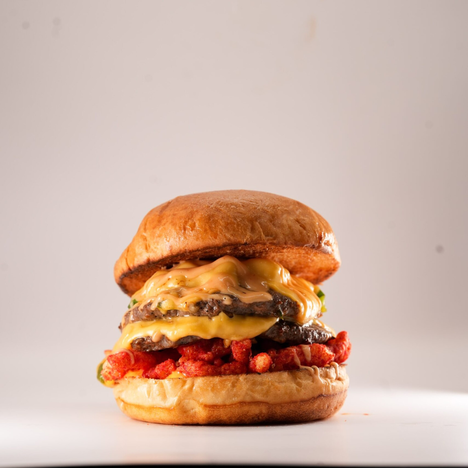 A double cheeseburger from The Burger Truck, topped with melted cheese, sauce, and crunchy red snacks.