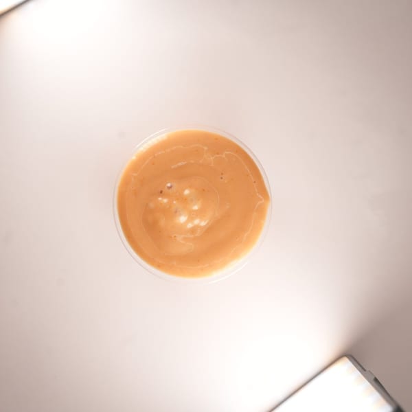 Top-down view of a small clear plastic cup filled with orange-brown burger sauce.