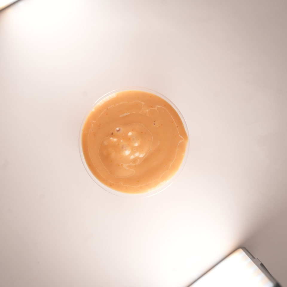 Top-down view of a small clear plastic cup filled with orange-brown burger sauce.
