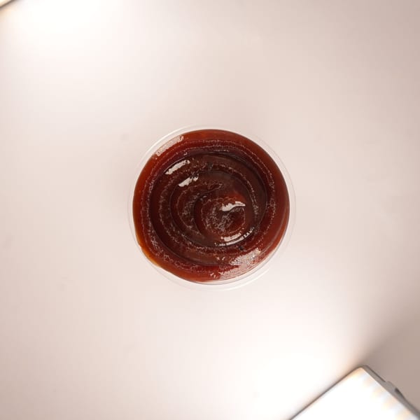 Overhead view of a clear plastic cup filled with dark brown barbecue sauce.
