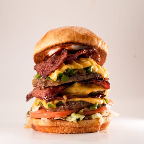 A towering triple-patty Burger Truck burger with bacon, cheese, jalapeños, tomato, and lettuce.