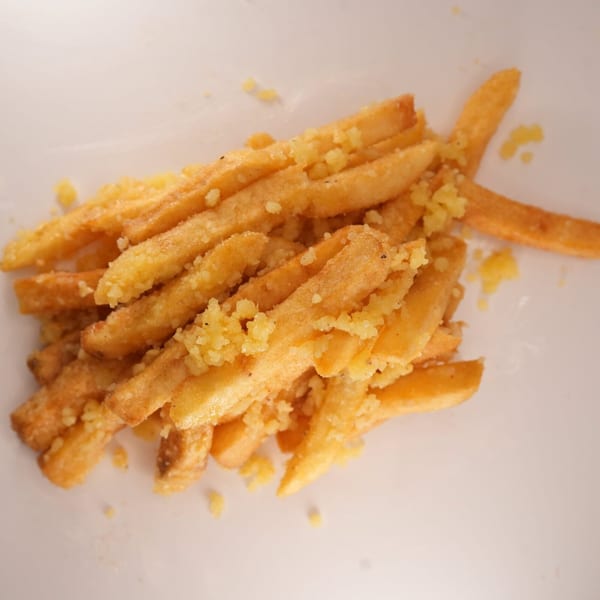 Close-up of golden french fries from The Burger Truck, generously topped with grated cheese.